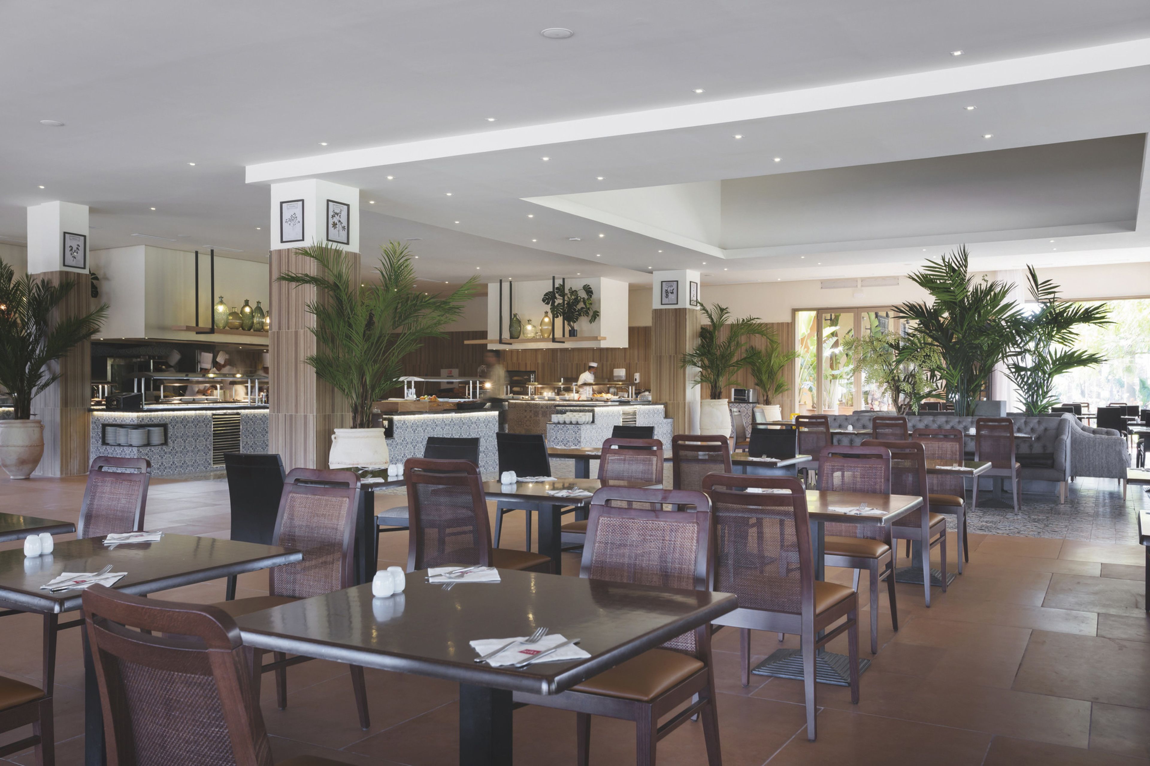 En rummelig restaurant med høje lofter, moderne møbler og et centralt køkkenområde.