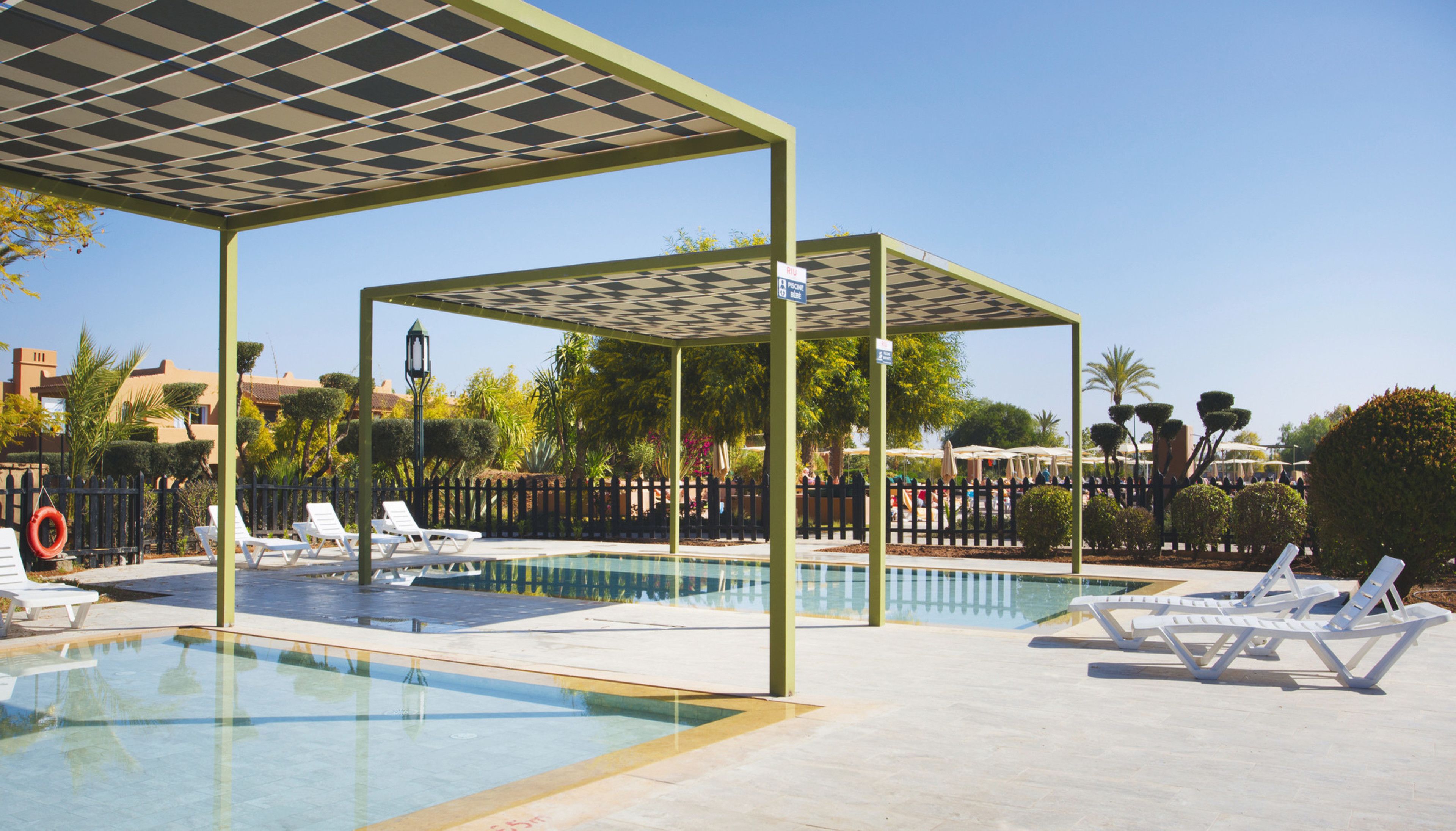 A pool area with lounge chairs, a covered seating area, and a fence.