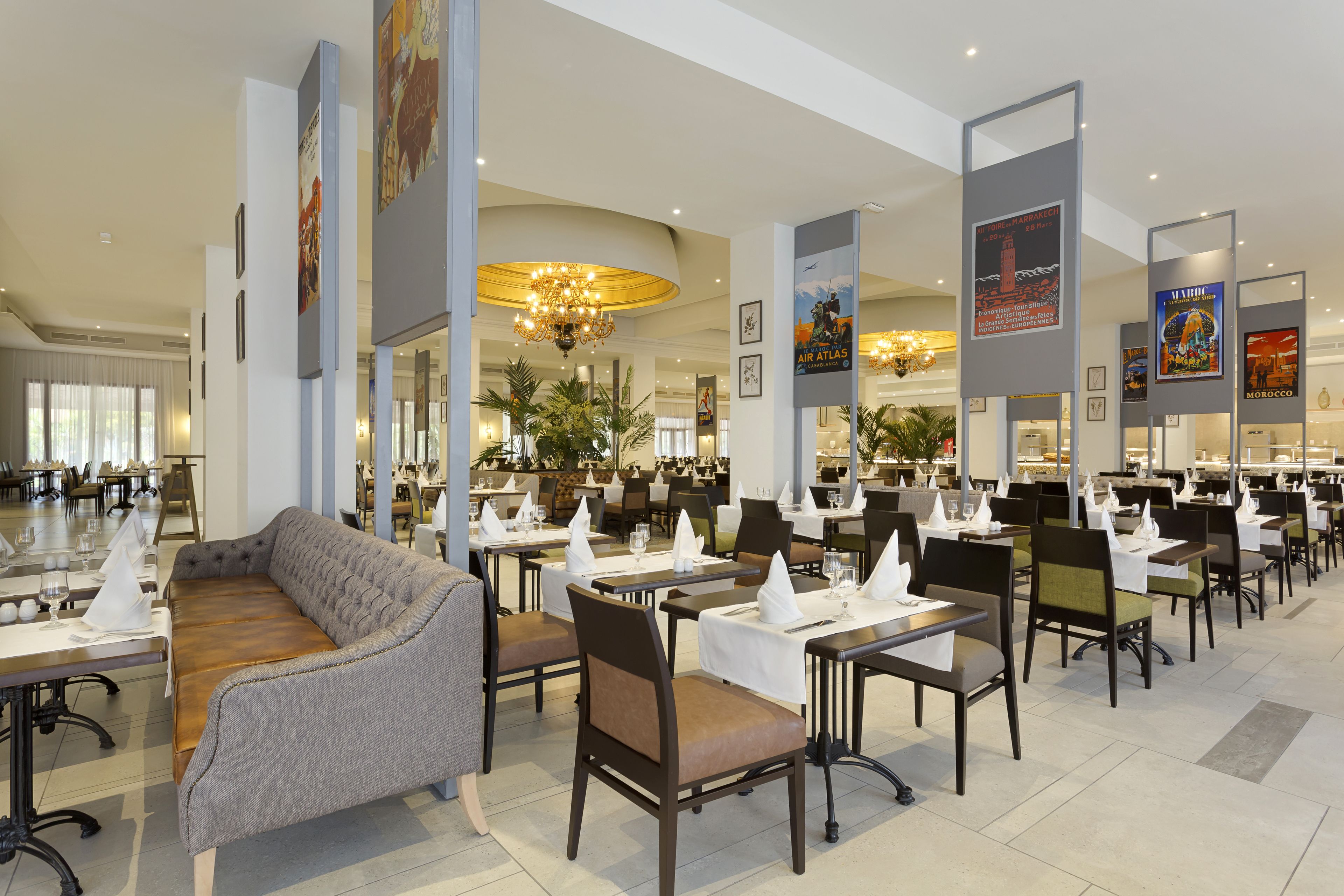 Een ruim restaurant met hoge plafonds, kroonluchters en diverse zitplaatsen, waaronder tafels en een bank.