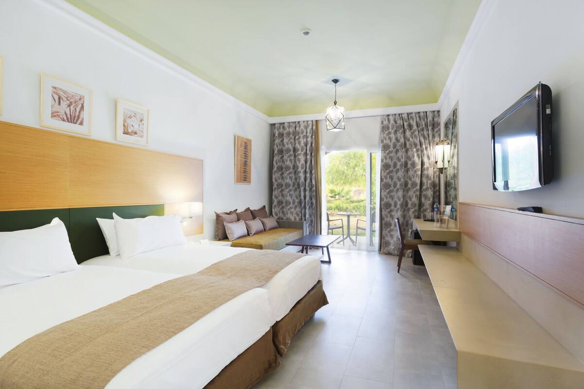 A hotel room with a large bed, a desk, a television, and a view of the outdoors.