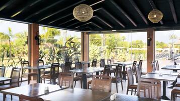 Un espace extérieur aménagé pour les repas, avec des tables et des chaises, de grandes fenêtres et des lampes décoratives en osier.