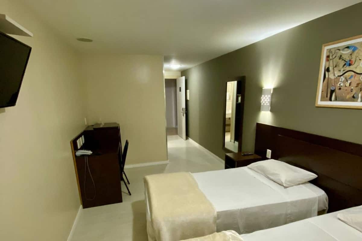Une chambre d’hôtel avec deux lits, un bureau, une chaise, une télévision et un tableau au mur.