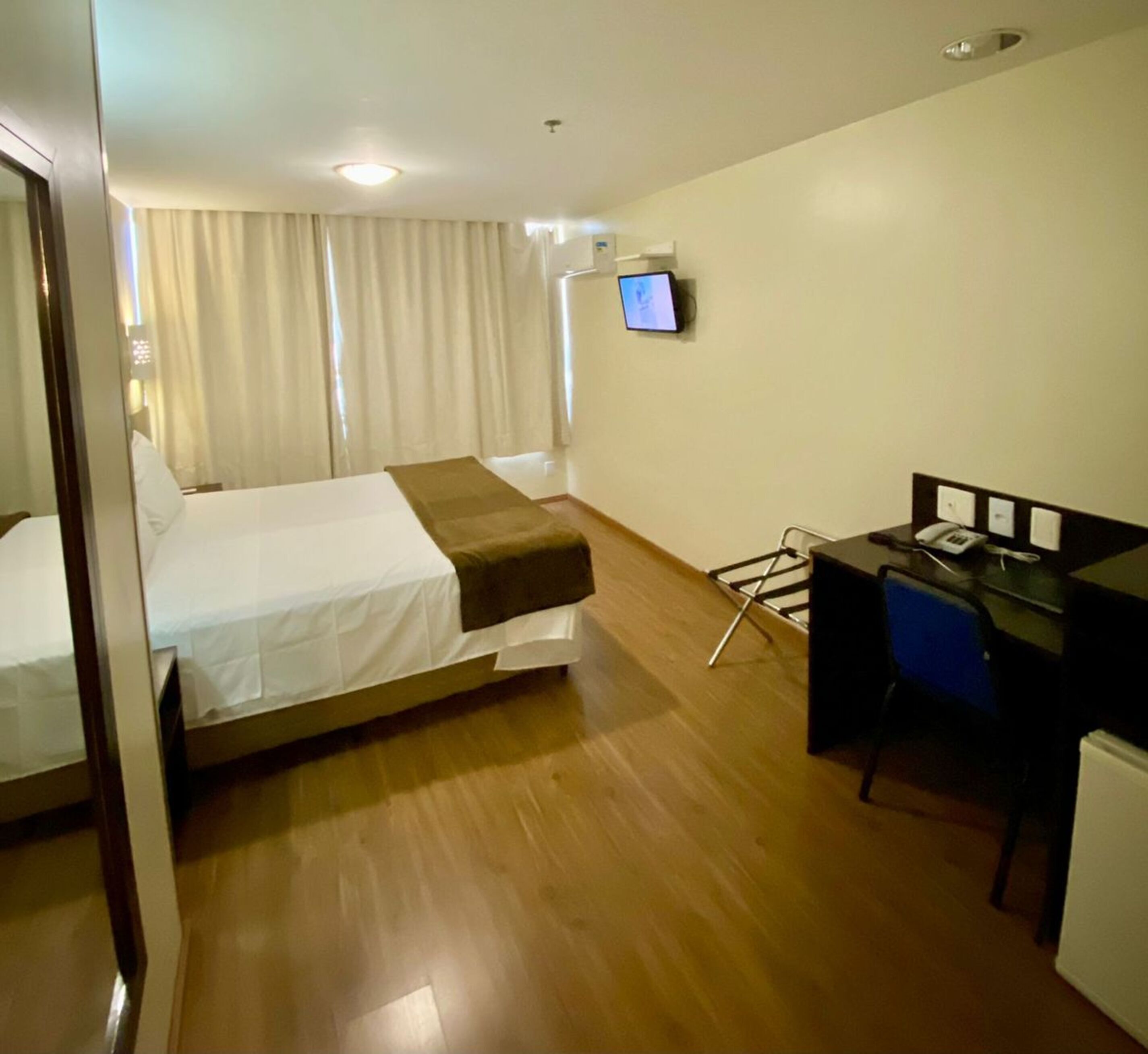 Una habitación de hotel con cama, escritorio, silla, televisor y un refrigerador pequeño.