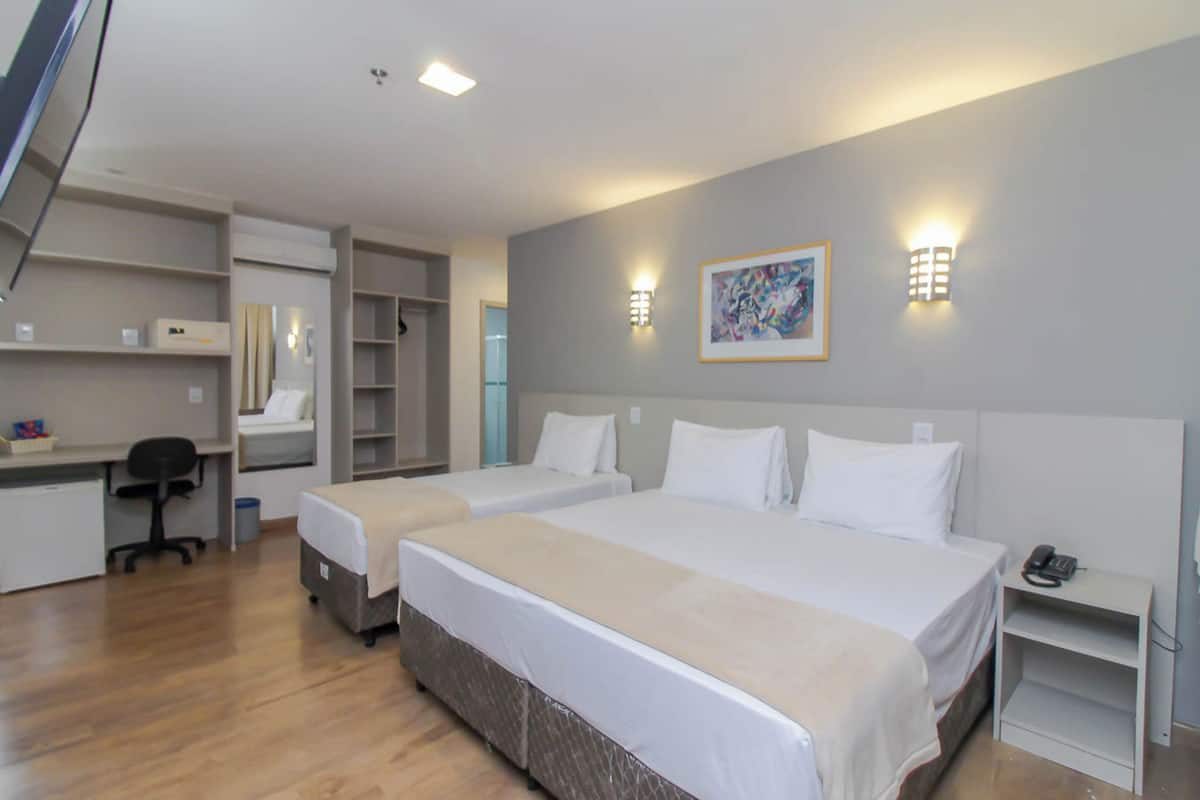 Une chambre d’hôtel avec deux lits, un bureau, une chaise, une armoire et un tableau au mur.