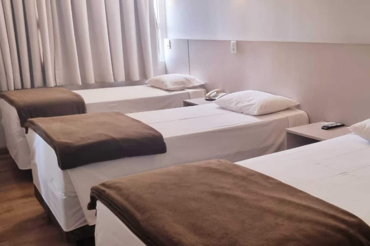Une chambre d’hôtel avec deux lits simples, chacun équipé d’un oreiller et d’une couverture. Il y a une table de chevet avec un téléphone et une télécommande.