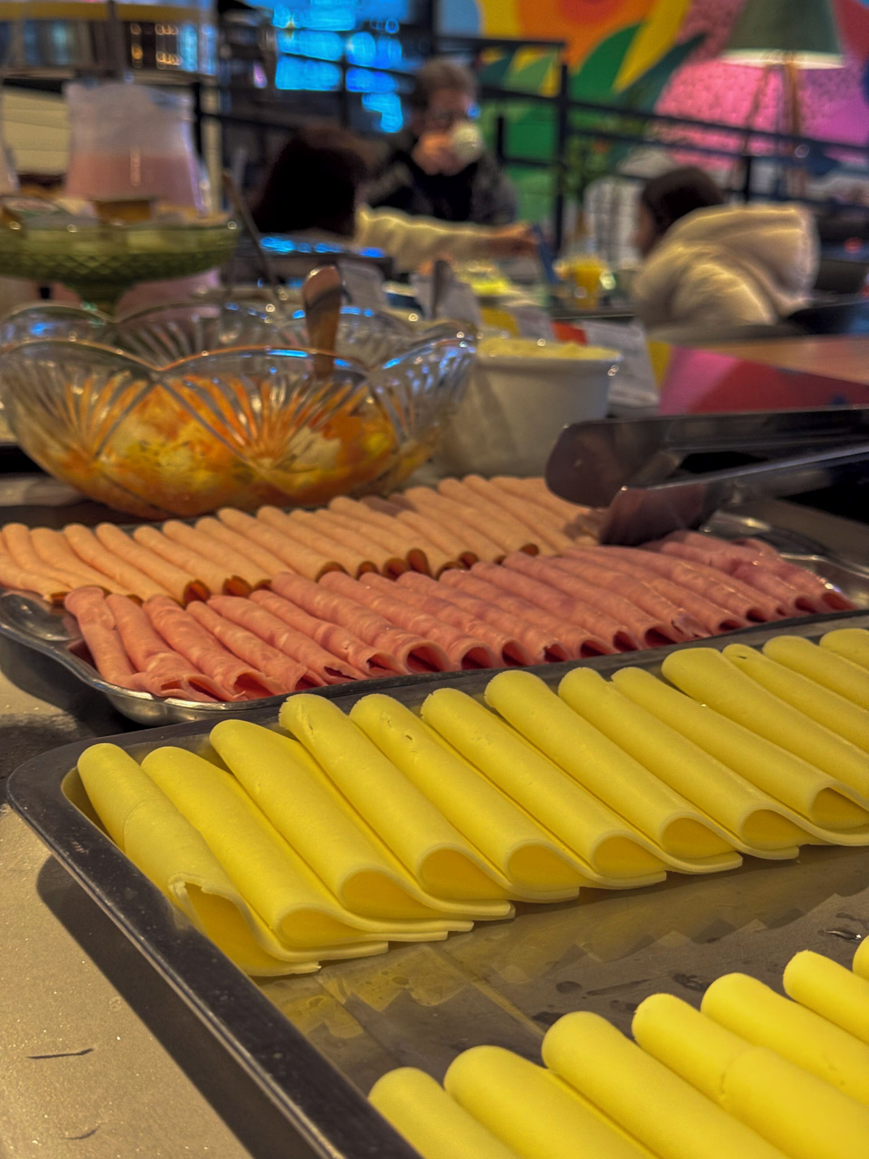 Mesa de buffet com diversos alimentos, incluindo fatias de carne e pães amarelos.