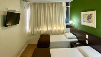 Une chambre d’hôtel avec deux lits, un téléviseur à écran plat fixé au mur, une fenêtre avec des rideaux et un mur d’accent de couleur verte.