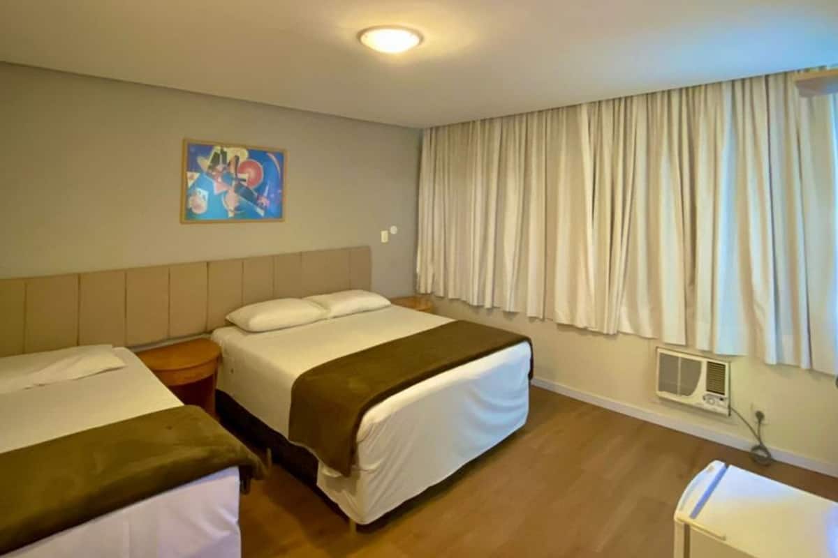 Une chambre d’hôtel avec deux lits, un tableau au mur, une fenêtre avec des rideaux et une petite table.