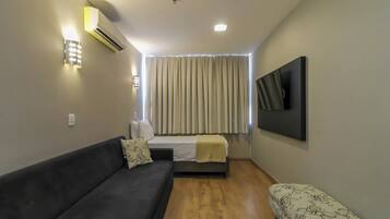 A compact room with a sofa, a bed, a small table, and a wall-mounted TV.