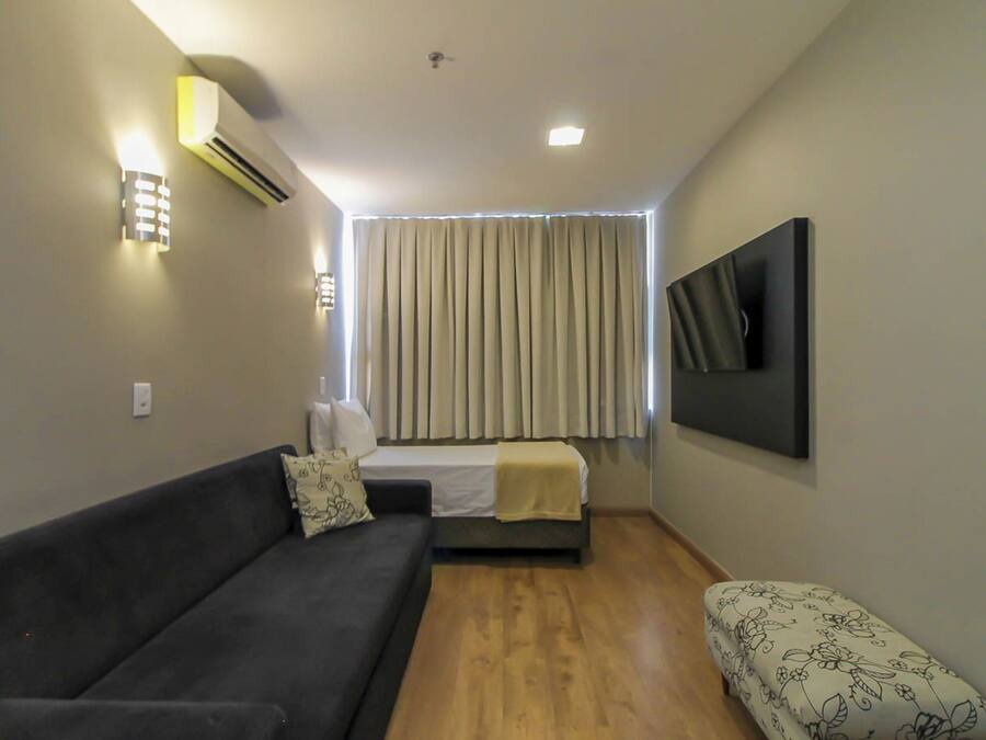 A compact room with a sofa, a bed, a small table, and a wall-mounted TV.