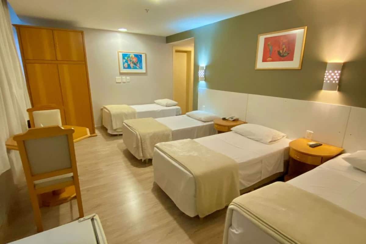 Une chambre d’hôtel avec quatre lits simples, une chaise en bois, un bureau et une petite table.