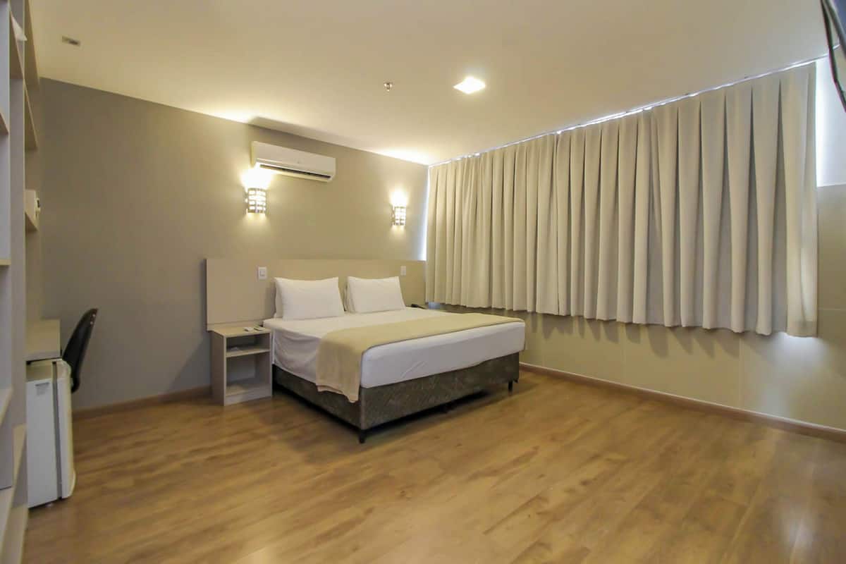 Une chambre d’hôtel équipée d’un lit, de tables de chevet, d’un appareil de climatisation et d’une fenêtre avec des rideaux.