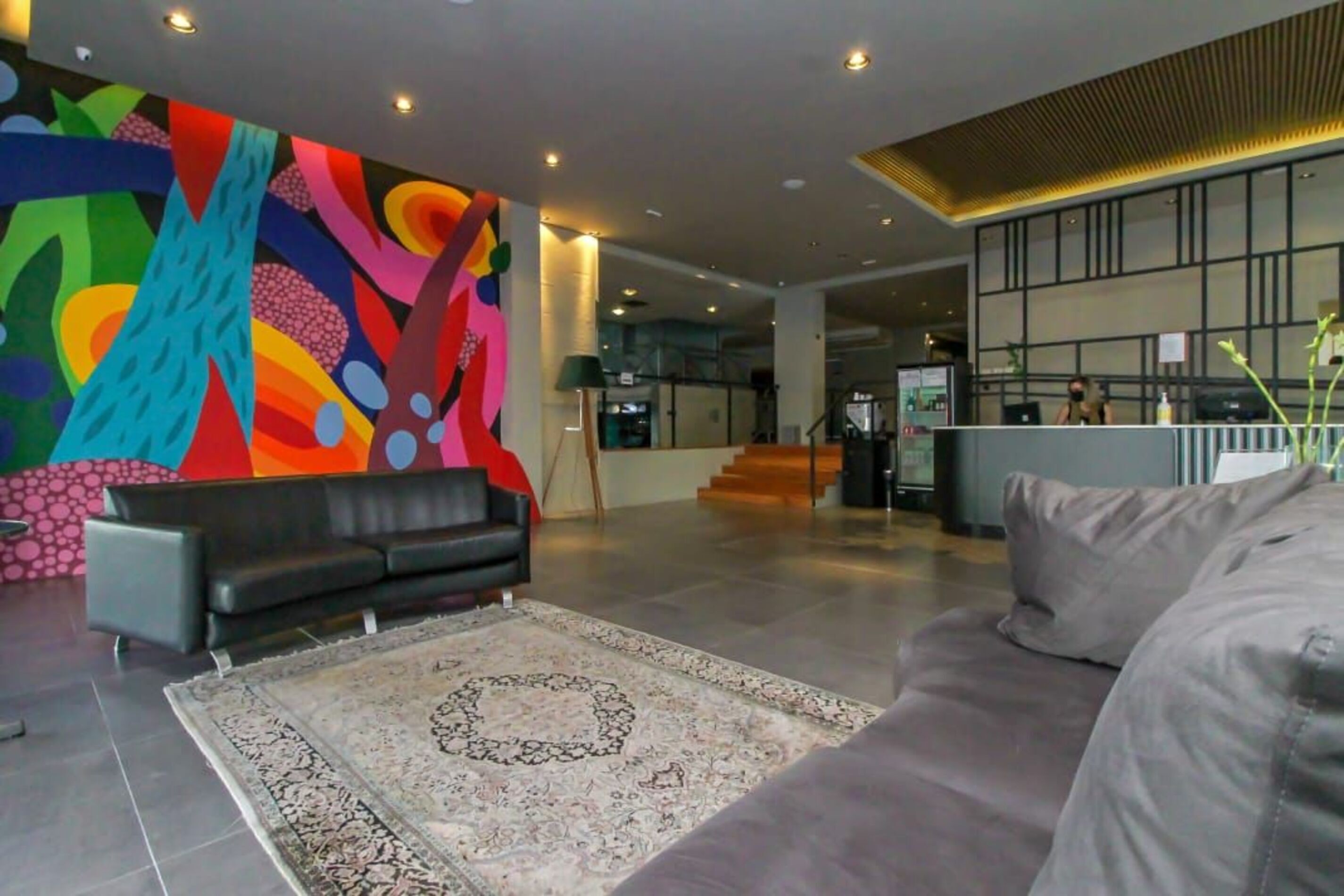 Un hall d’entrée moderne agrémenté d’une fresque murale abstraite aux couleurs vives, d’un canapé gris, d’un tapis à motifs et d’un escalier menant à un étage supérieur.