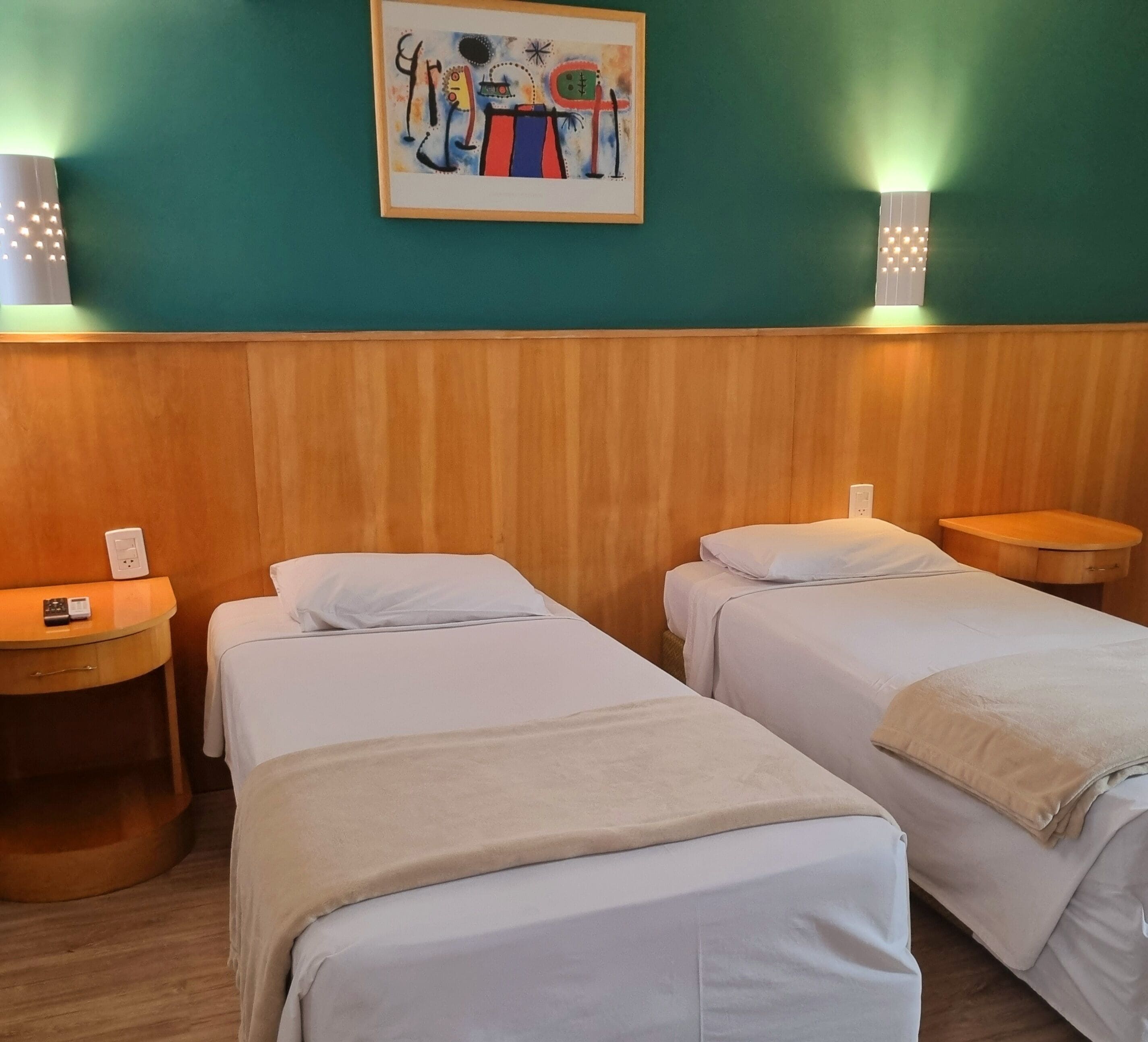 Une chambre d’hôtel avec deux lits simples, une tête de lit en bois, un tableau au mur et des lampes de chevet.