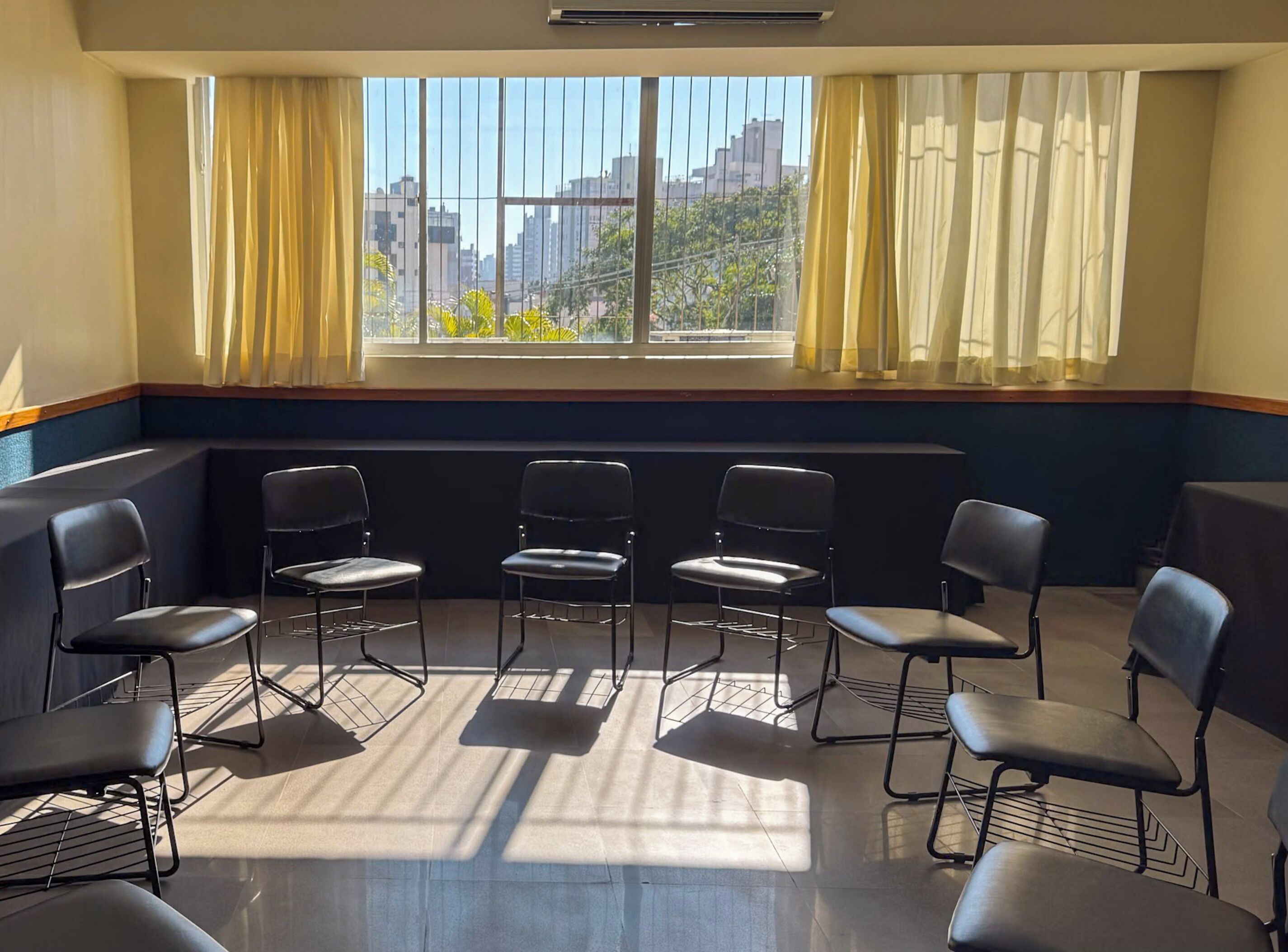 Una habitación con un ventanal grande, cuatro sillas dispuestas en semicírculo y un radiador debajo de la ventana.