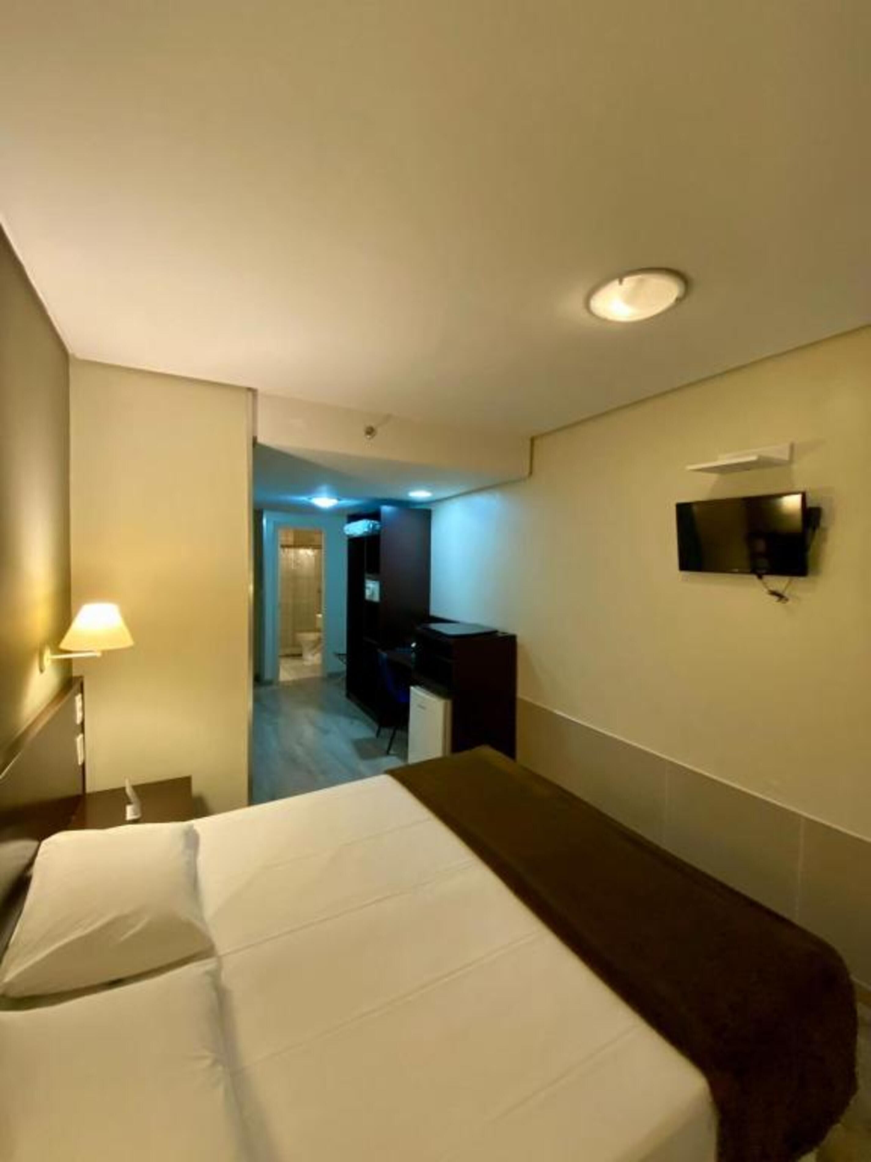 Une chambre d’hôtel équipée d’un lit, d’un bureau, d’une chaise, d’un téléviseur fixé au mur et d’une lampe.