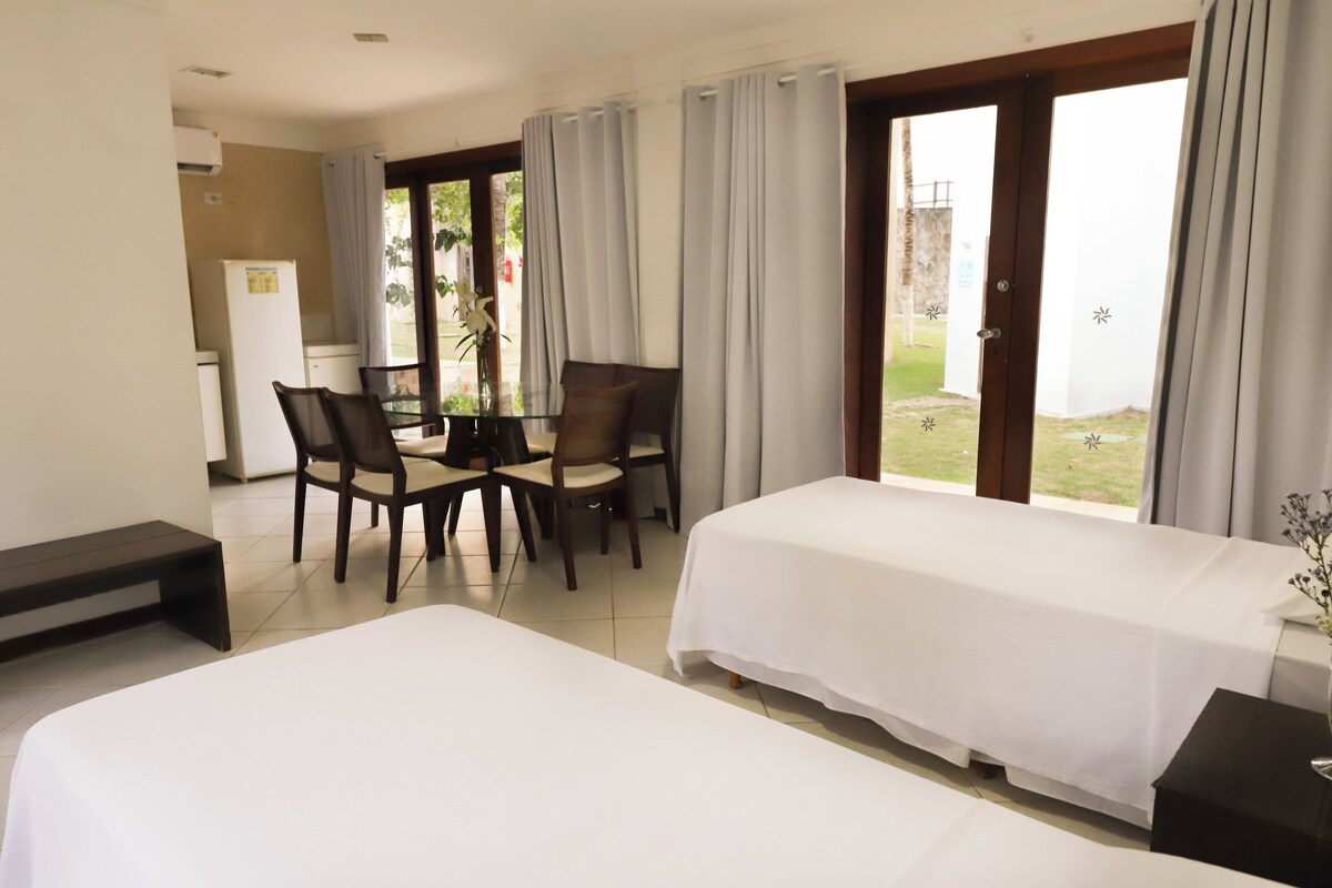 Ein Hotelzimmer mit zwei Betten, einem Esstisch mit Stühlen, einem Kühlschrank und Blick ins Freie.