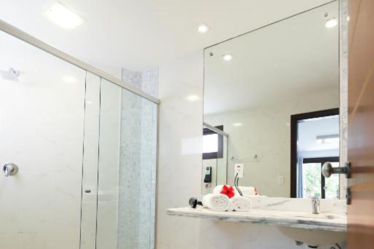 Ein modernes Badezimmer mit Duschkabine aus Glas, einer weißen Toilette mit einer roten Blume und einem großen Spiegel über dem Waschbecken.