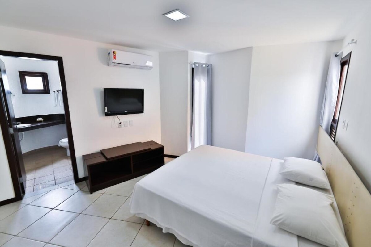 Ein Hotelzimmer mit Bett, einem an der Wand befestigten Fernseher, einem Badezimmer mit Toilette und Waschbecken sowie einer Duschkabine.