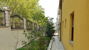 A narrow courtyard with a stone pathway, potted plants, and a yellow building with barred windows. - Guest House Vlado (Split)