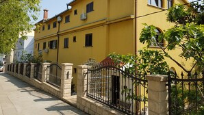 A yellow building with a gated entrance, multiple windows, and a clear sky. - Guest House Vlado (Split)