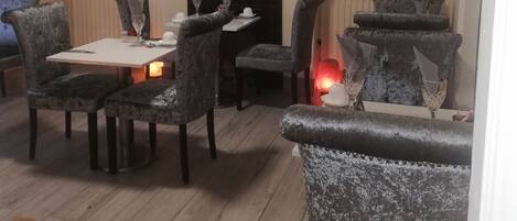 A dining area with a fireplace, a mirrored wall, and a shelf with bottles.