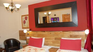 Quarto de hotel com duas camas, cabeceira de madeira, parede vermelha, lustre, televisão e espelho.