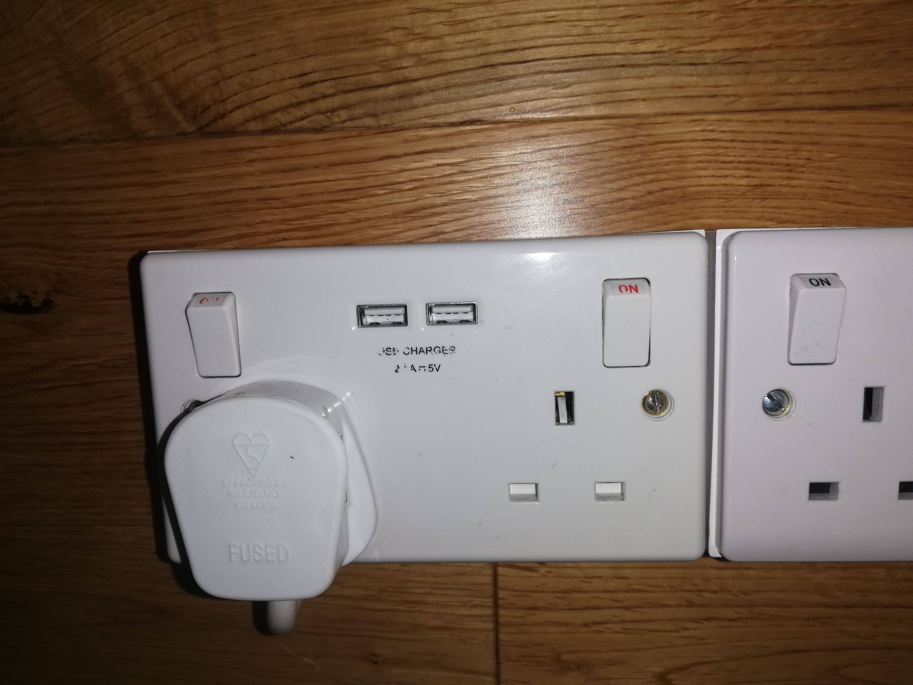Un enchufe blanco con un puerto USB, un tomacorriente estándar y un interruptor etiquetado como 'ON'.