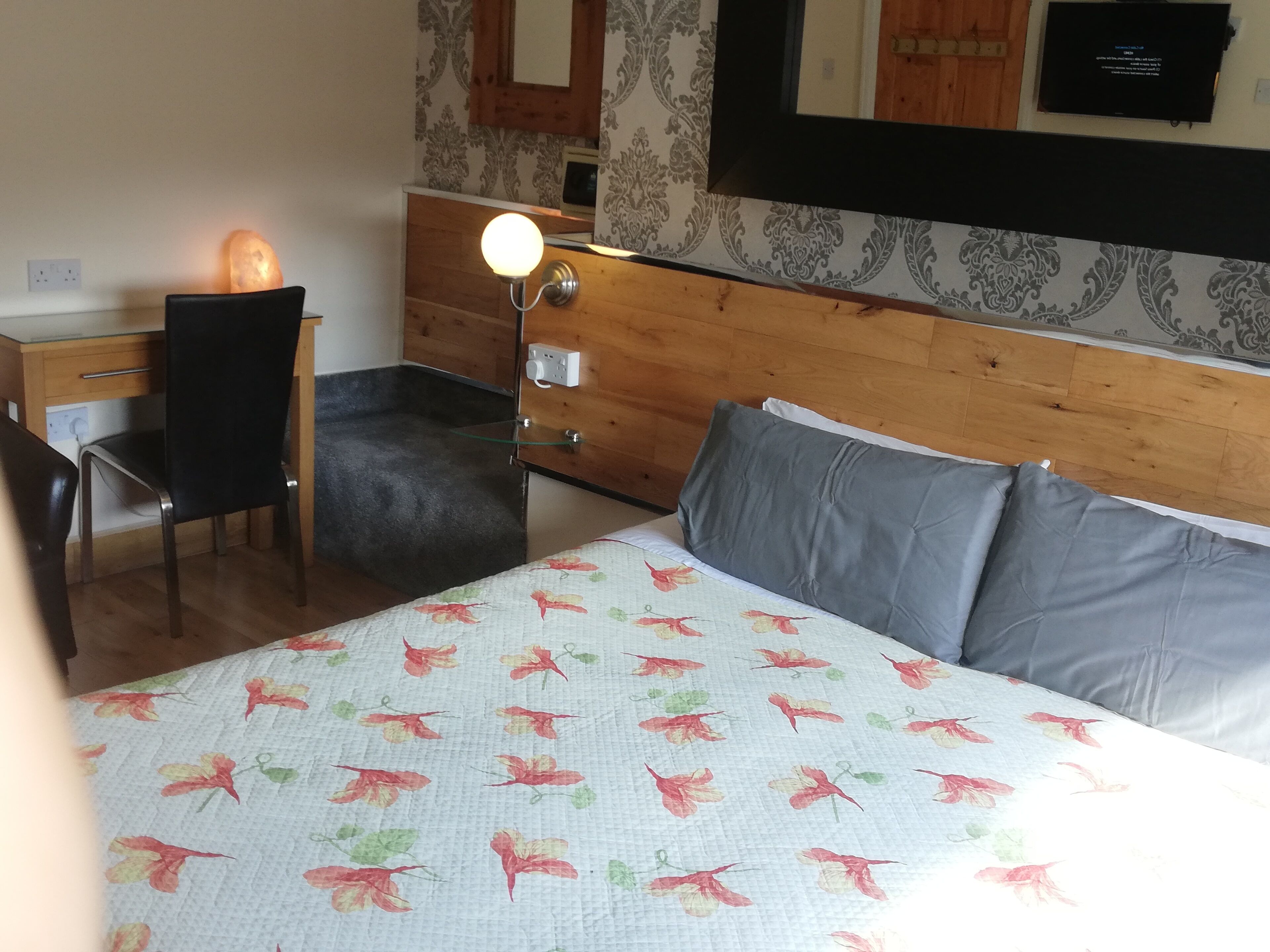 A bedroom with a bed, a desk, a chair, a nightstand, and a lamp.
