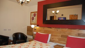 Ein Hotelzimmer mit einem hölzernen Kopfteil, zwei Betten mit blumigen Überwürfen, einer roten Akzentwand, einem Spiegel und einem Fernseher.