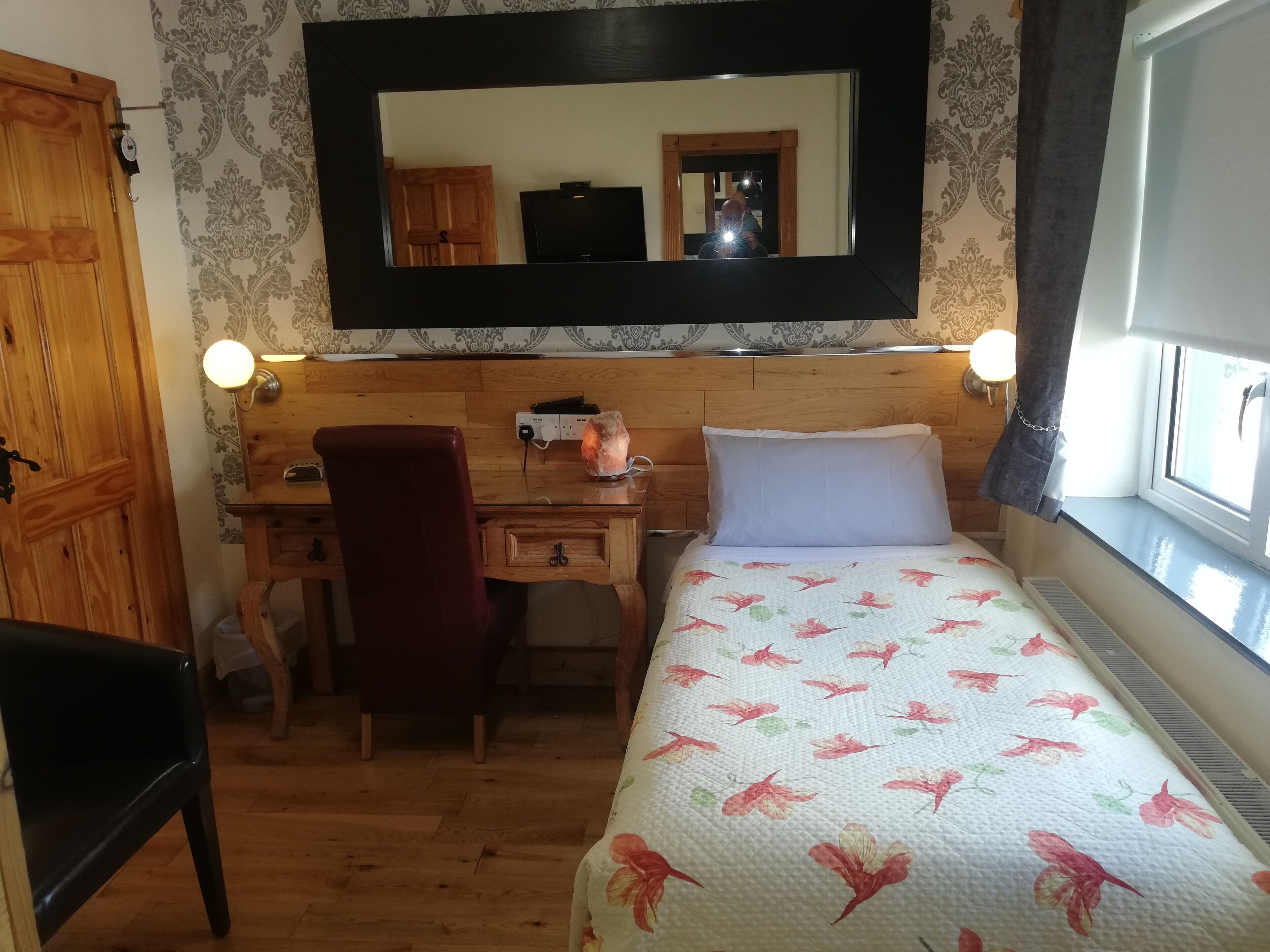 A bedroom with a wooden desk, chair, and bed with floral bedding.