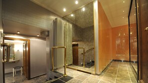 Un moderno vestíbulo de hotel con piso de mármol, una escalera con barandas doradas, un espejo y una planta en maceta.