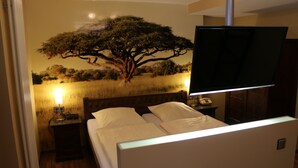 Habitación de hotel con cama, mesita de noche, lámpara, teléfono y televisor montado en la pared.