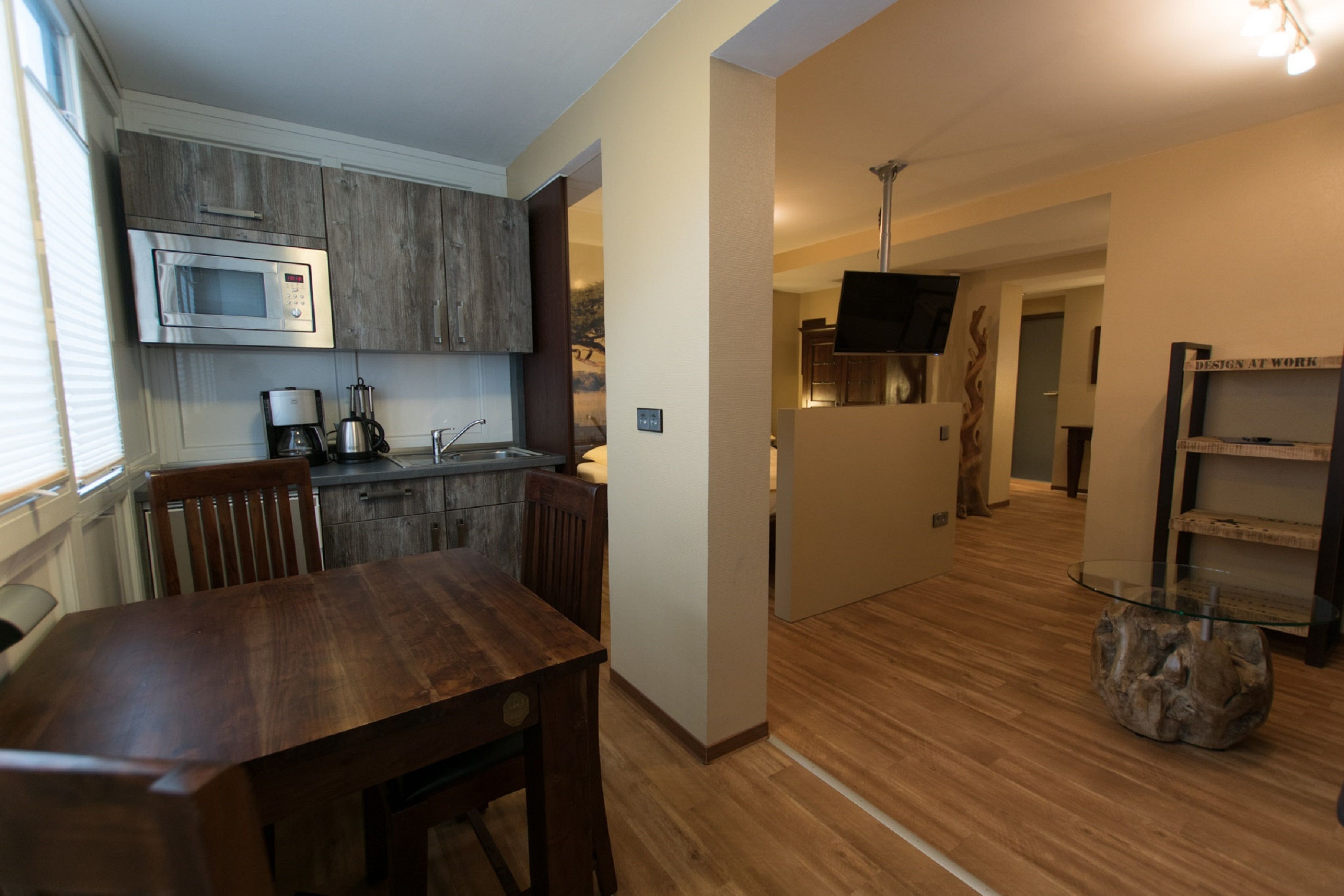A modern kitchen with a microwave, coffee maker, and wooden cabinets. There is a dining table and chairs in the foreground.