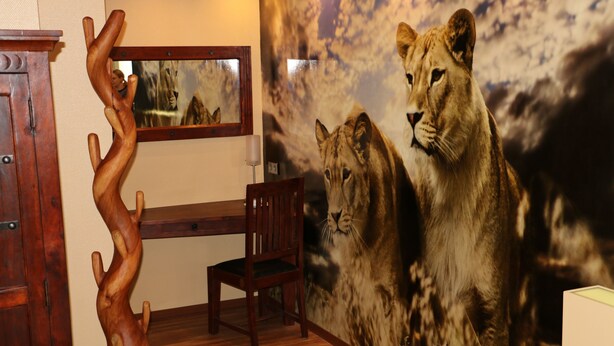 Una habitación con un armario de madera, una silla de madera y un mural en la pared con leones.