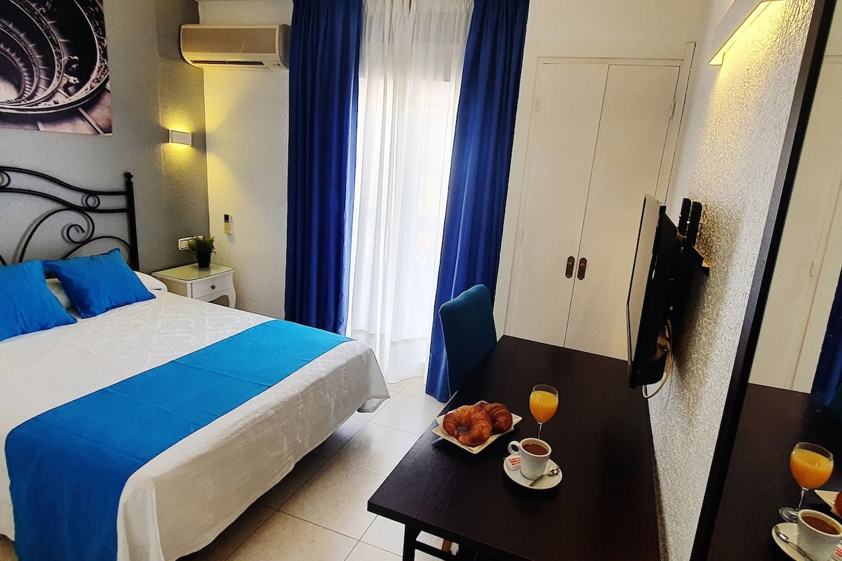 A hotel room with a bed, a table with breakfast, and a wardrobe.