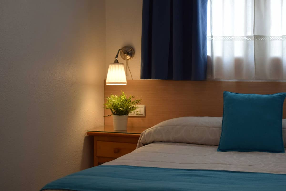 A neatly made bed with a blue pillow and a bedside table with a lamp and a potted plant.