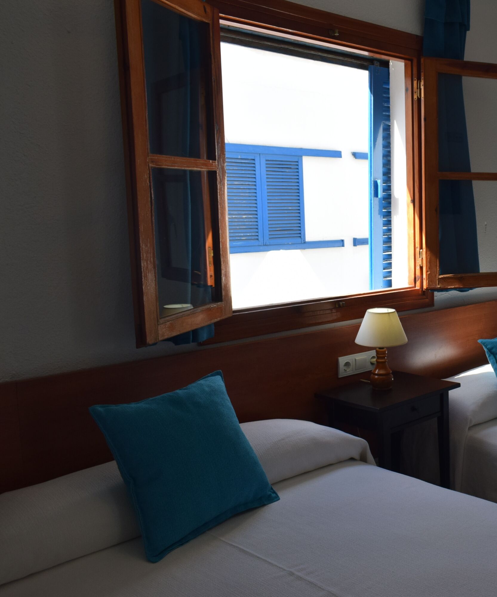 Une chambre d’hôtel avec un lit, une table de chevet avec une lampe et une fenêtre avec des volets bleus.