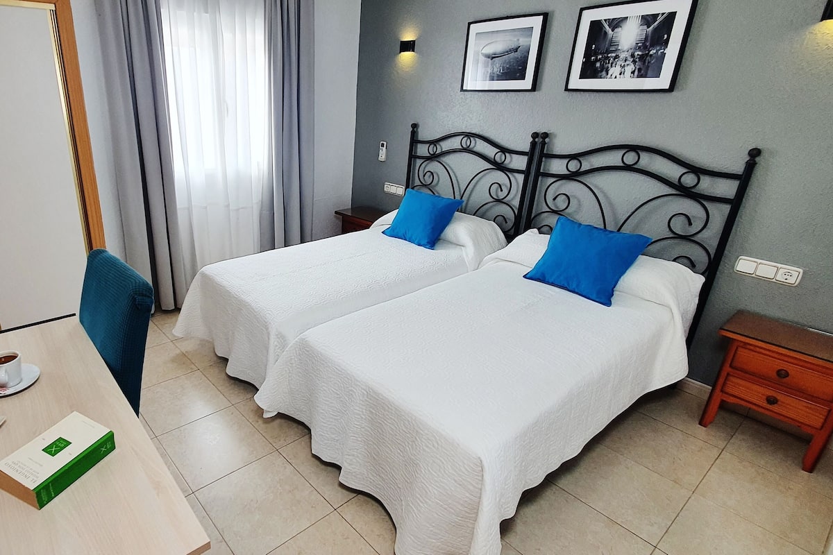 A hotel room with two beds, a table with breakfast, and a view of the street.