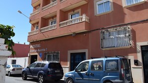 Un edificio con balcones, un cartel que dice "Hostal Juan de Austria I" y coches aparcados.
