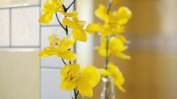 A bathroom with a white sink and a mirror reflecting a vase with yellow flowers.