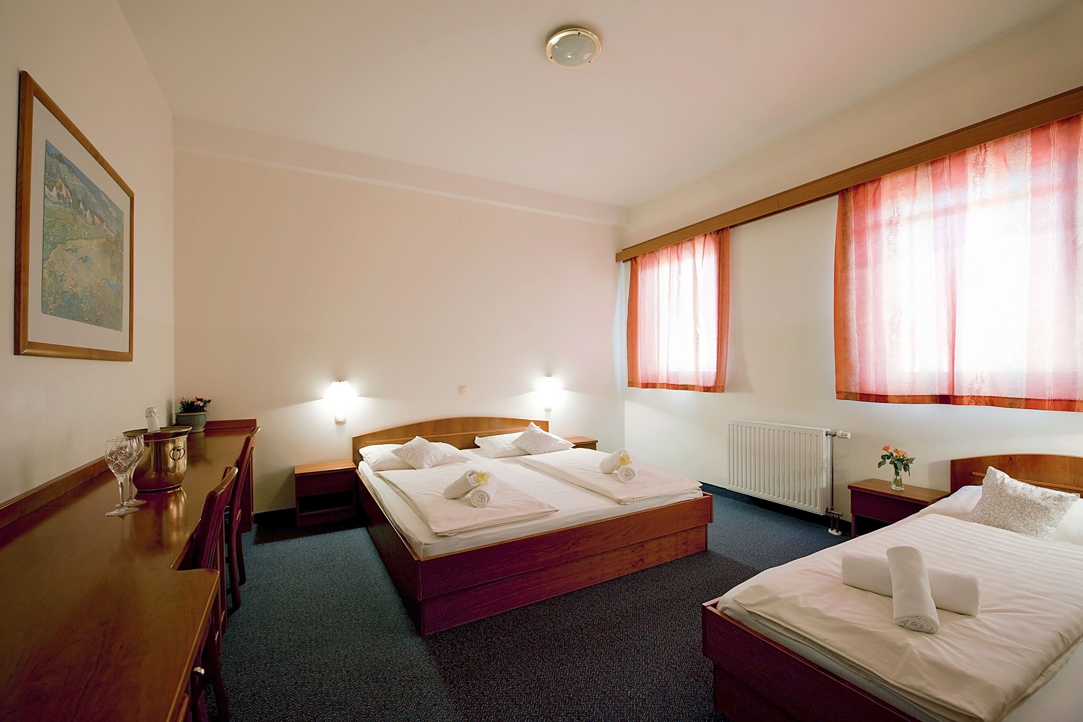 A hotel room with two beds, a wooden dresser, a table with a vase, and a painting on the wall.