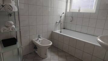 A bathroom with a bidet, a glass shower enclosure, a sink, and a window with blinds.