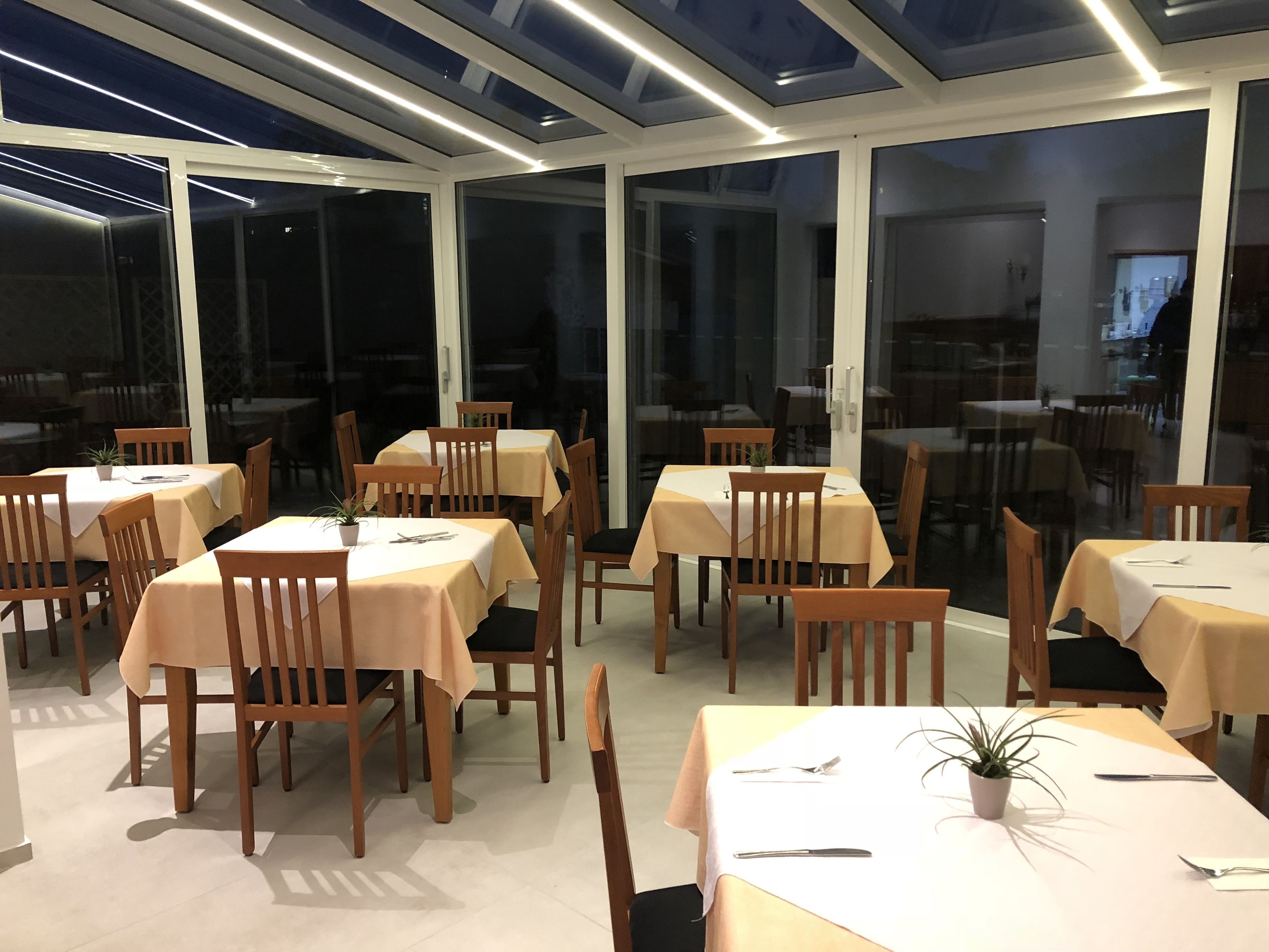 Un restaurante con mesas y sillas dispuestas en su interior, amplios ventanales y un diseño de techo moderno.