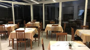 Un restaurante con mesas y sillas dispuestas en su interior, amplios ventanales y un diseño de techo moderno.