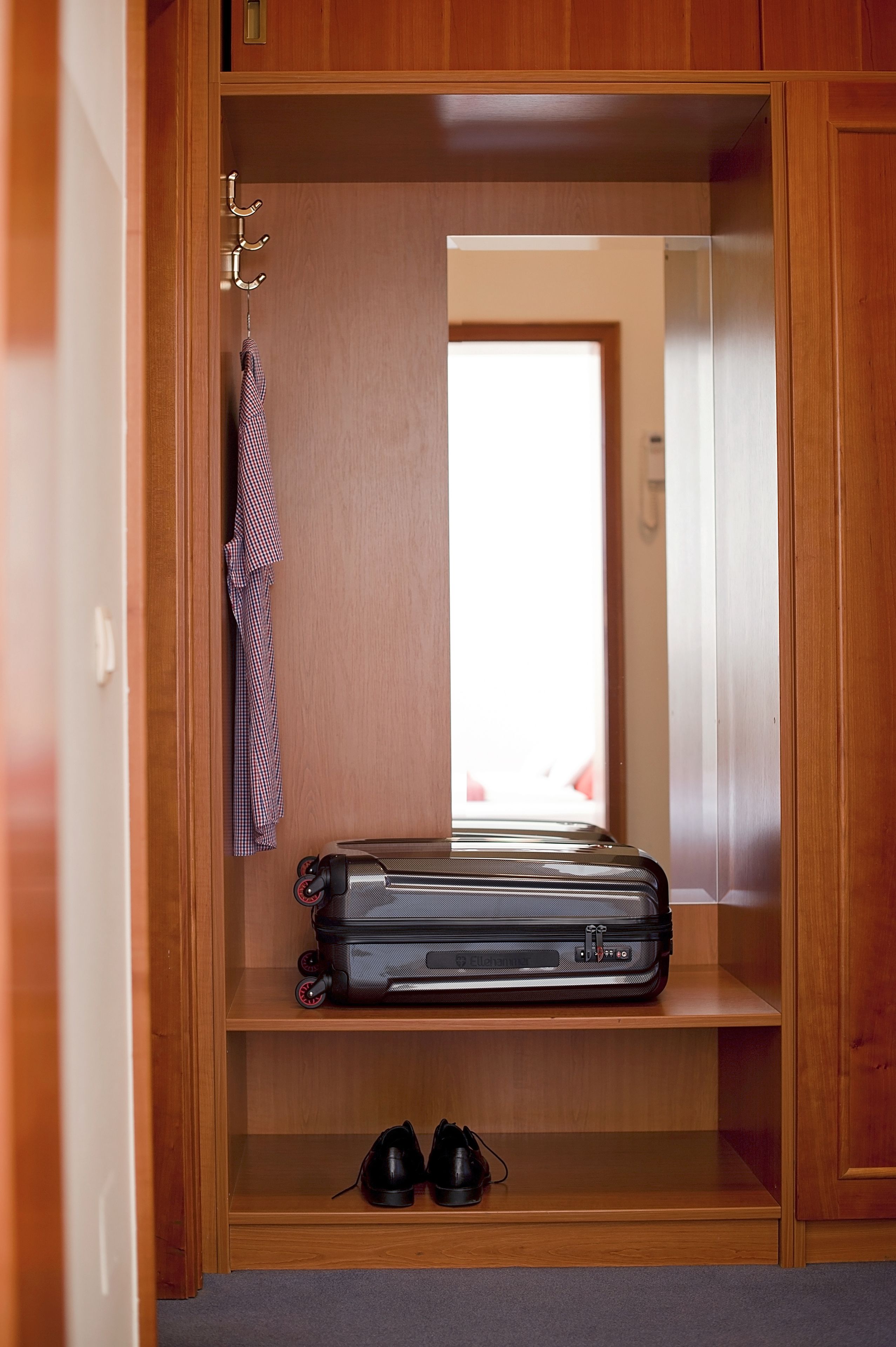 A wooden wardrobe with a suitcase and shoes inside.