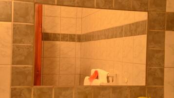 Un baño con ducha en esquina, paredes de azulejos y una puerta de madera.