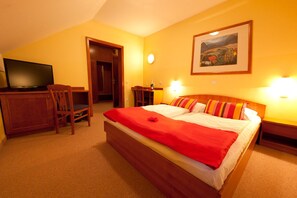 Una habitación de hotel con cama, escritorio con televisor y un cuadro en la pared.