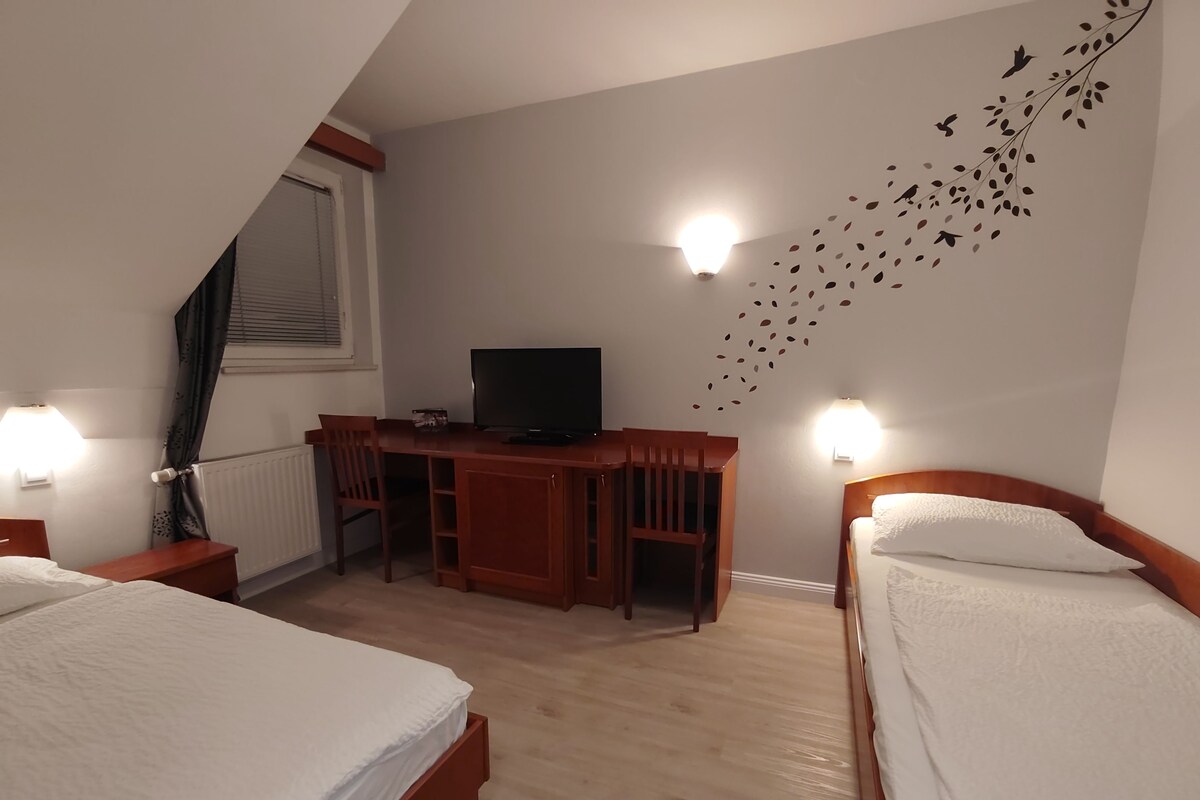 Una habitación de hotel con dos camas, un escritorio con televisor y luces fijadas a la pared.