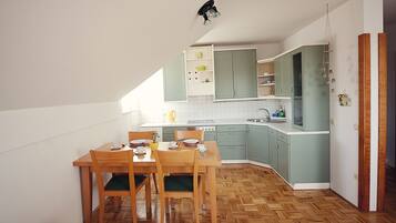 Una cocina compacta con piso de madera, una mesa de comedor con sillas y armarios de color verde claro.